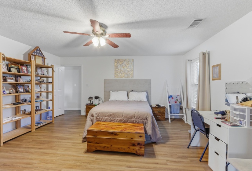 Spacious room featuring wood-finish flooring, a ceiling fan with integrated lighting, white walls, and a window with blinds and curtains