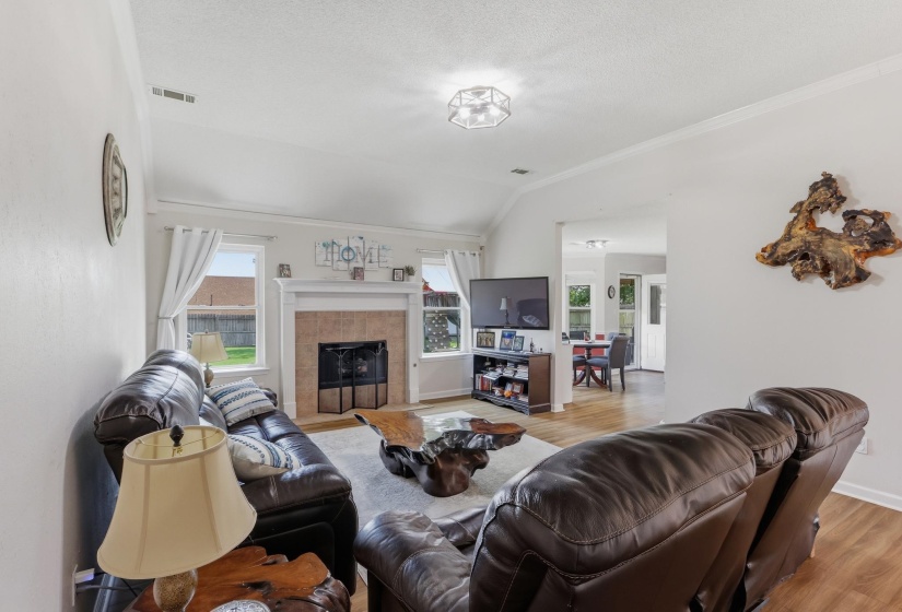 Living area featuring a vaulted ceiling, a fireplace with a tile surround and white mantel, and wood-finish flooring