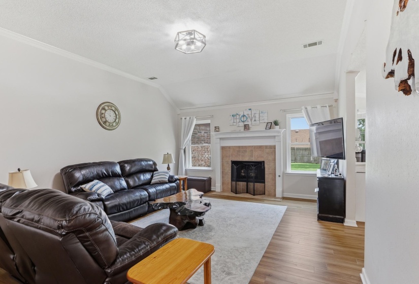 Living area featuring wood-finish flooring, a vaulted ceiling, and a fireplace with a tile surround and white mantle