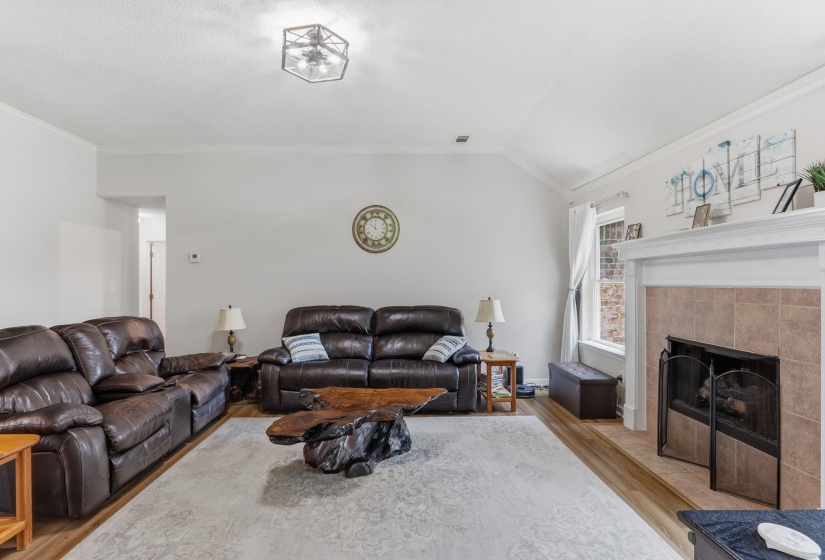 Living area featuring vaulted ceilings, crown molding, wood-finish flooring, a tile-surround fireplace with a white mantel, and a multi-light ceiling fixture