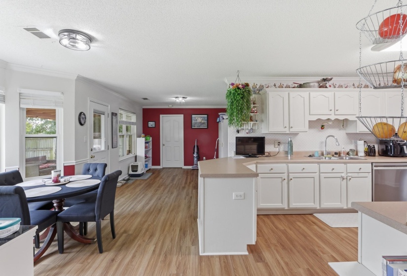 Kitchen and dining area featuring wood-finish flooring, white cabinetry, a light-toned countertop, stainless steel appliances, and a double-pane window
