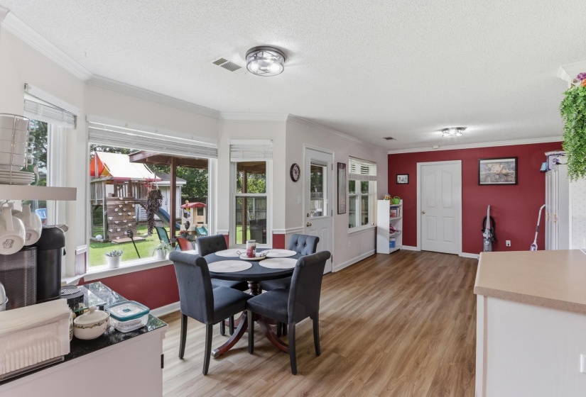Open-concept living area featuring wood-finish flooring, a vibrant accent wall, recessed lighting, and a bay window overlooking a green space