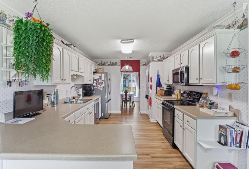 Galley kitchen featuring wood-finish flooring, white cabinetry, and light-toned countertops