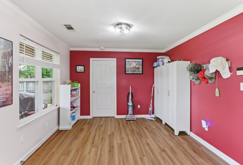 Room featuring wood-finish flooring, white crown molding, and a prominent window with horizontal blinds