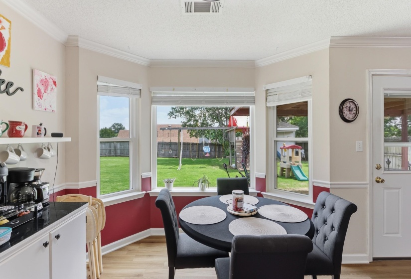 Bay window dining area with wood-finish flooring, crown molding, and two-tone wall treatment