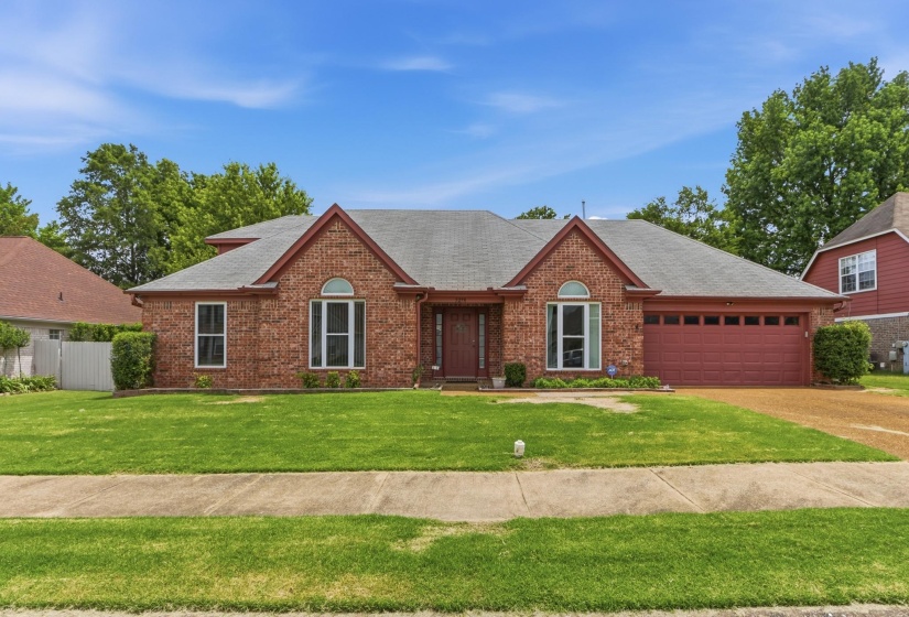Traditional brick residence featuring a prominent gabled roofline, an arched entry window, and a two-car garage with a matching red door