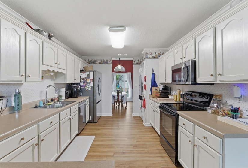 Galley kitchen featuring light wood-finish flooring, white cabinetry with crown molding, and neutral countertops
