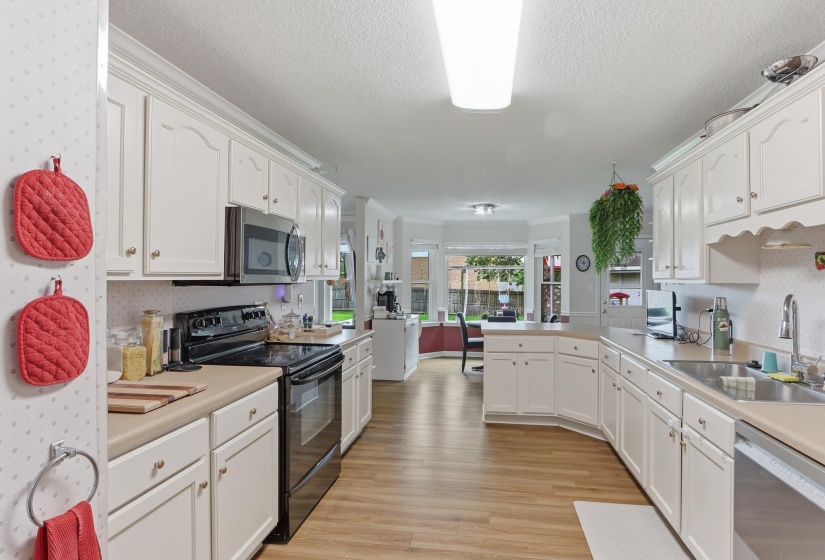 Kitchen featuring white cabinetry with crown molding, laminate countertops, wood-finish flooring, and a stainless steel dishwasher