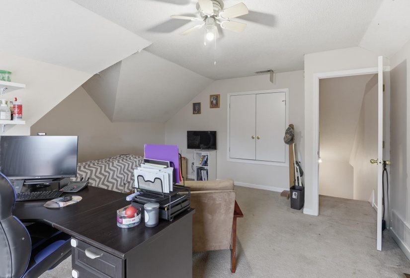 Versatile attic space featuring sloped ceilings, ceiling fan, carpet flooring, a built-in closet with double bifold doors, and an open doorway leading to a staircase