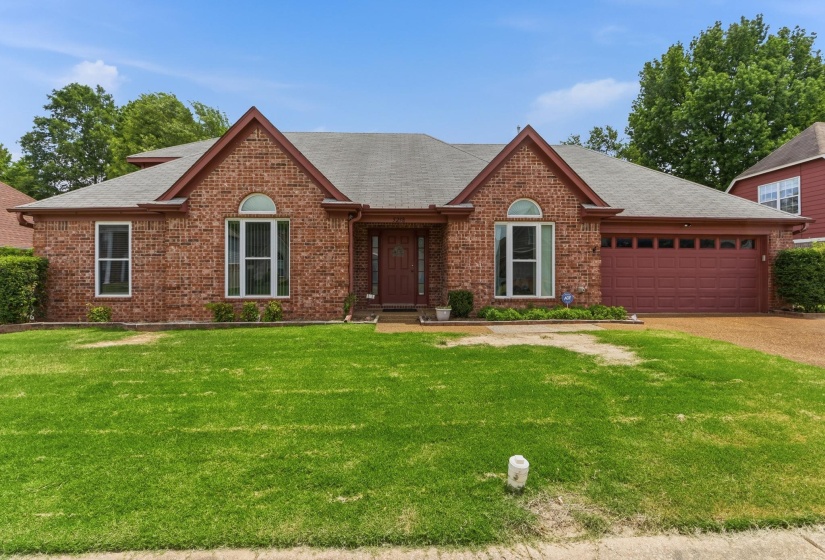 Brick facade residence featuring a front lawn and an attached two-car garage with a red door