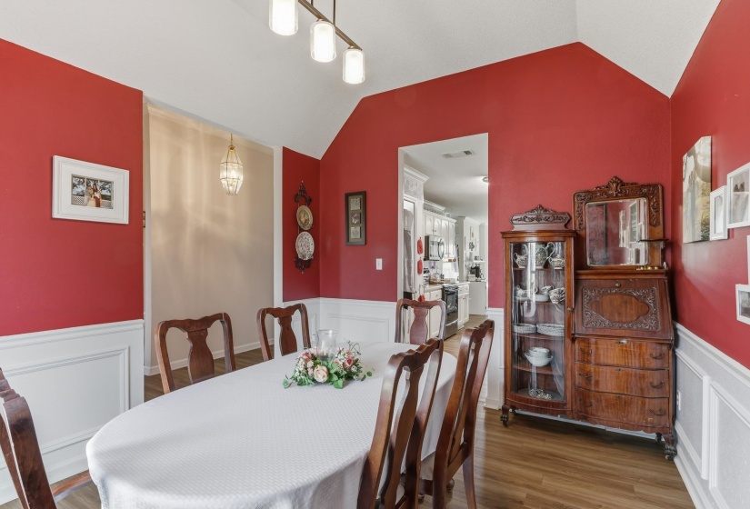 Formal dining area featuring vaulted ceilings, wood-finish flooring, and white wainscoting