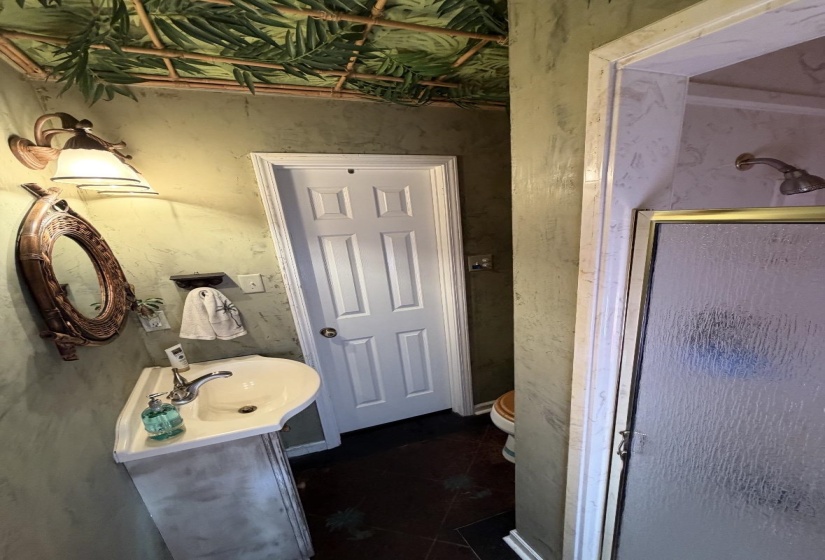Compact bathroom featuring a pedestal sink, wall-mounted light fixture, decorative mirror, and a shower with a clear glass enclosure inside of guest house