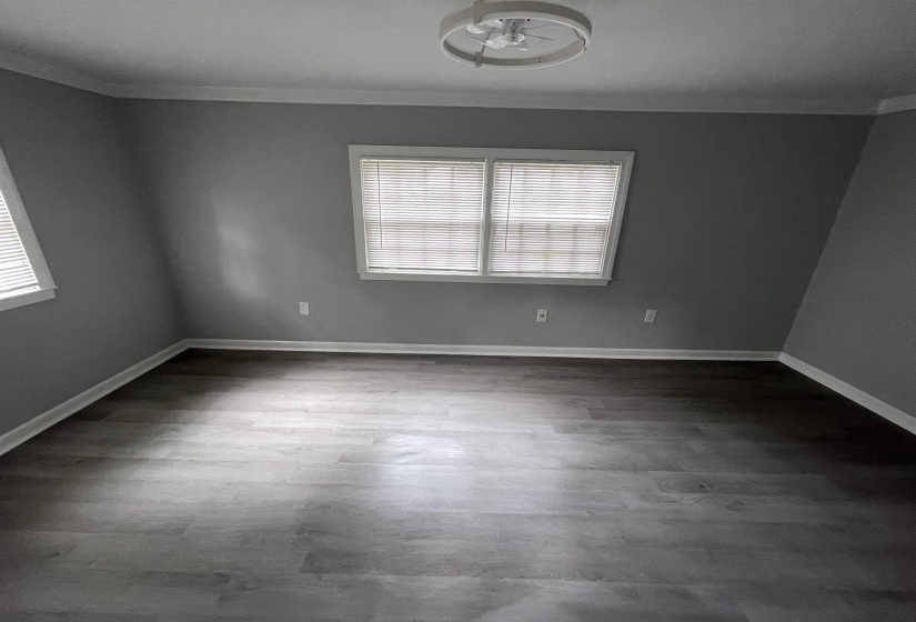 Spacious room featuring wood-finish flooring, two windows with blinds, a modern ceiling light fixture, and crown molding
