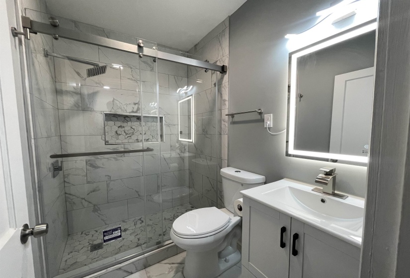 Full bathroom featuring a frameless glass shower enclosure with a rain shower head, marble-look tile walls, and a recessed hexagonal tile niche