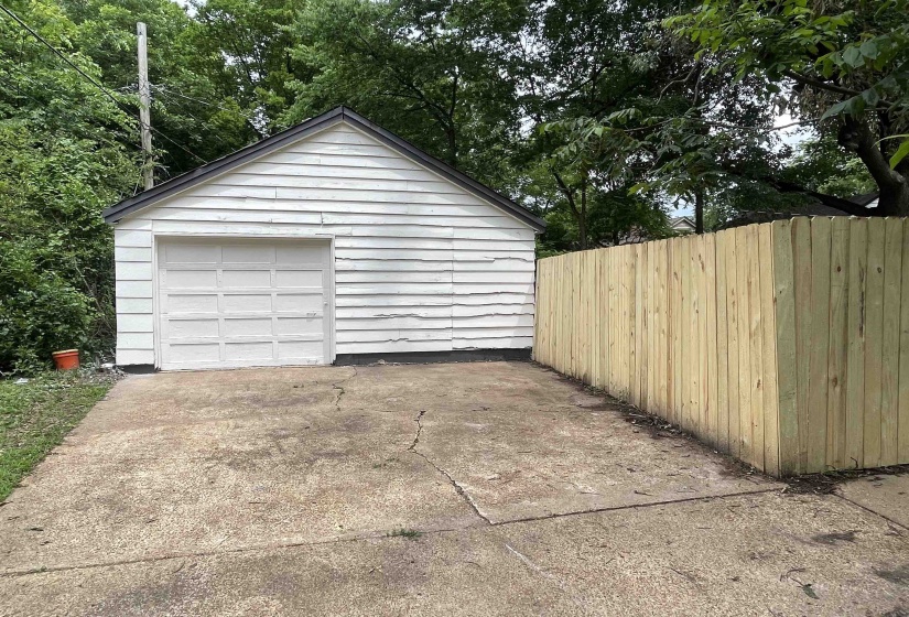 Detached garage with white siding and a new wood privacy fence