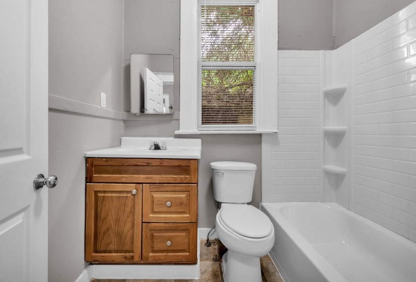 Bathroom featuring a wood-finish vanity with a white countertop and integrated sink, a white toilet, and a white bathtub with subway tile-style surround and integrated shelving