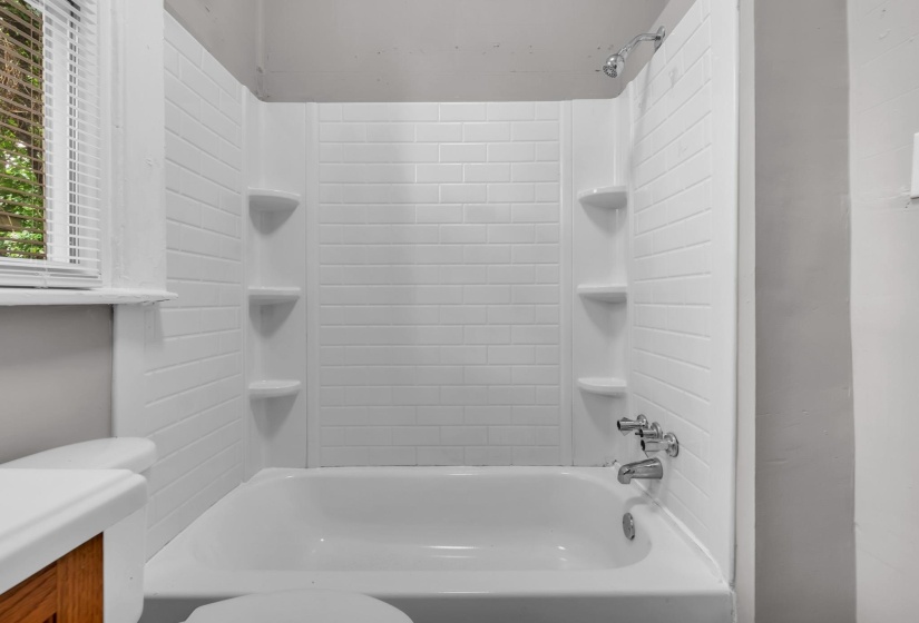 White bathtub with integrated shower, chrome fixtures, and a white subway tile-patterned surround