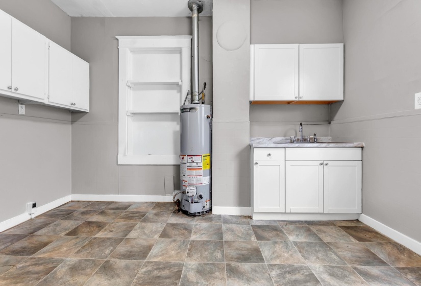 Utility space featuring a water heater, white cabinetry, a sink with a countertop, and patterned floor tiling