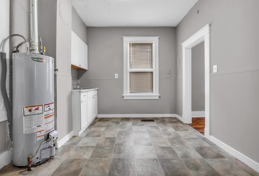 Utility area featuring a water heater, gray wall finishes, and geometric tile flooring