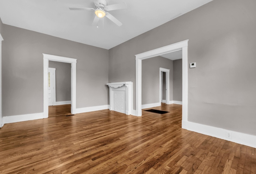 Spacious room featuring wood-finish flooring, a decorative white fireplace surround, and a ceiling fan with integrated lighting