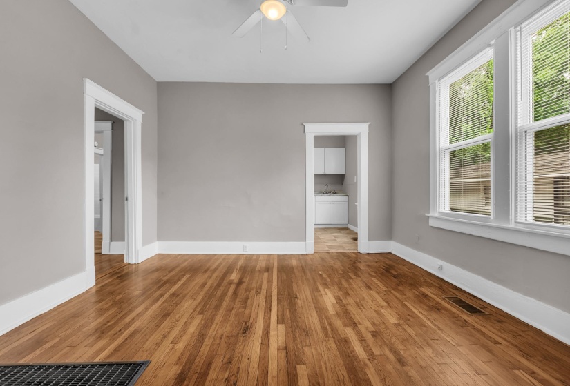 Spacious room featuring wood-finish flooring, light grey painted walls, white trim, and a ceiling fan with integrated lighting