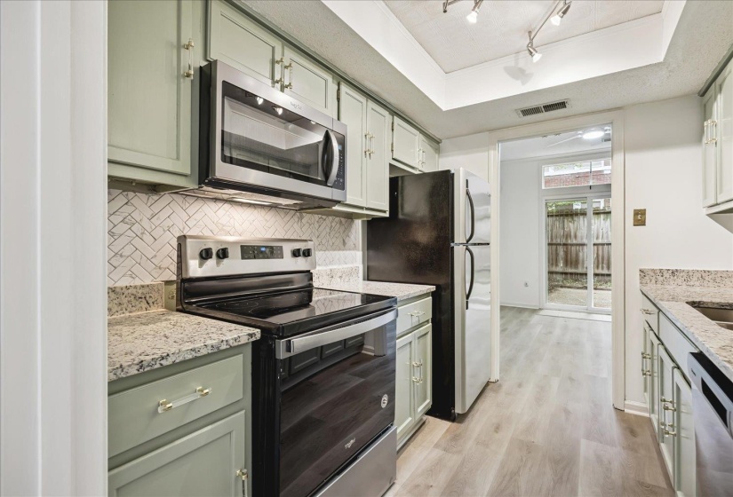 Kitchen featuring light green cabinetry, granite-finish countertops, stainless steel appliances, and wood-finish flooring