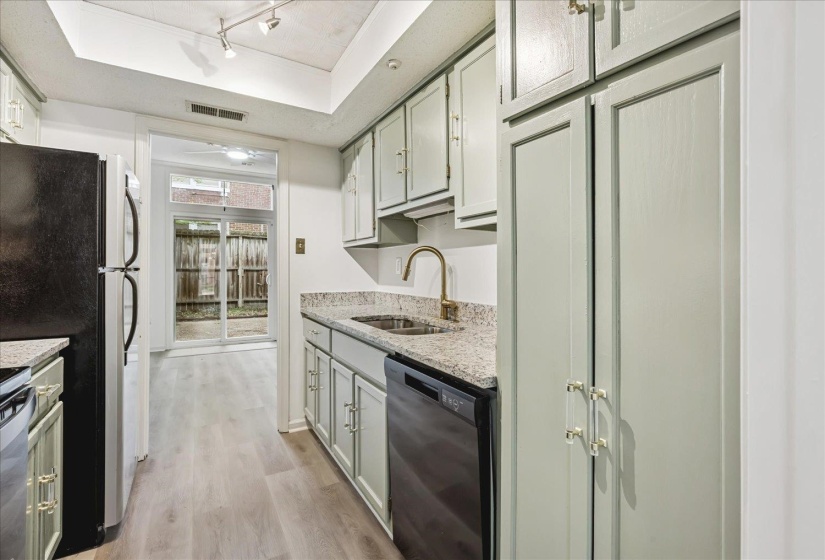 Kitchen featuring light green cabinetry, granite-style countertops, stainless steel sink with gold-tone faucet, and wood-finish flooring