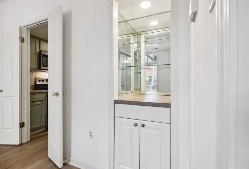 Built-in wet bar featuring mirrored backing, glass shelving, and lower cabinetry with a stone-finish countertop