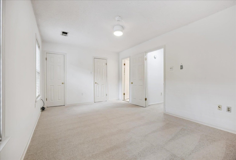 Spacious room featuring neutral carpeting, white walls, multiple doorways, a window with blinds, and a ceiling fan with integrated lighting