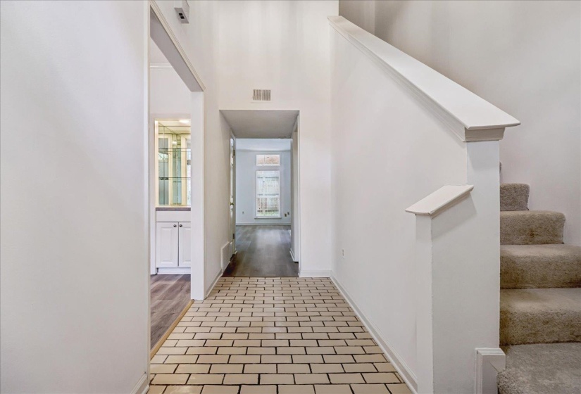 Entryway featuring brick-patterned tile flooring, a carpeted staircase, and high ceilings