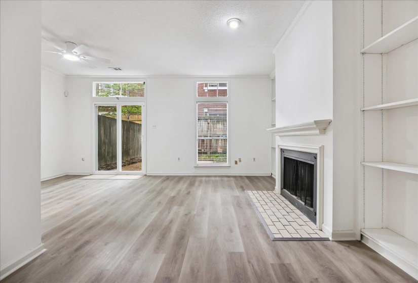 Spacious interior featuring wood-finish flooring, a fireplace with a tiled hearth, built-in shelving, a ceiling fan, and a glass sliding door