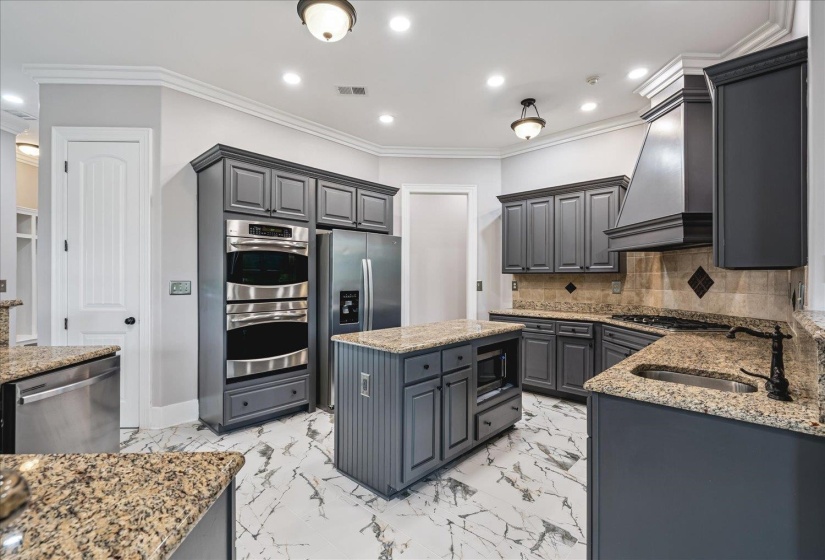Kitchen featuring dark gray cabinetry, granite countertops, stainless steel appliances, a center island with built-in microwave, and marble-look tile flooring