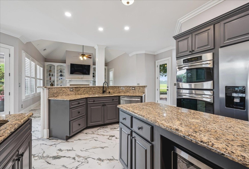 Open-concept kitchen featuring granite countertops, built-in stainless steel appliances, dark wood-finish cabinetry, and marble-look tile flooring