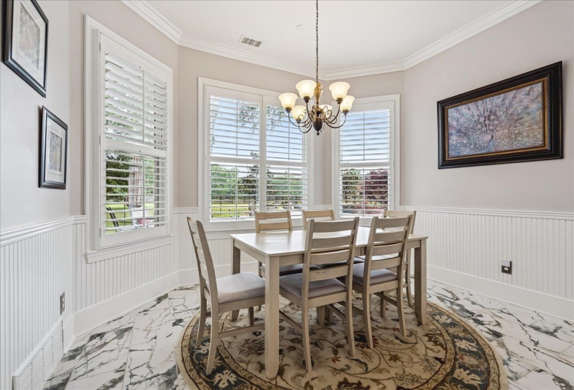 Dining area featuring multiple windows with plantation shutters, beadboard wainscoting, crown molding, and a five-light chandelier