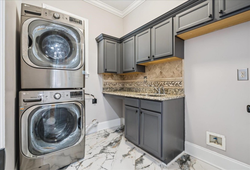 Laundry area featuring stacked appliances, dark cabinetry, and a countertop with an integrated sink