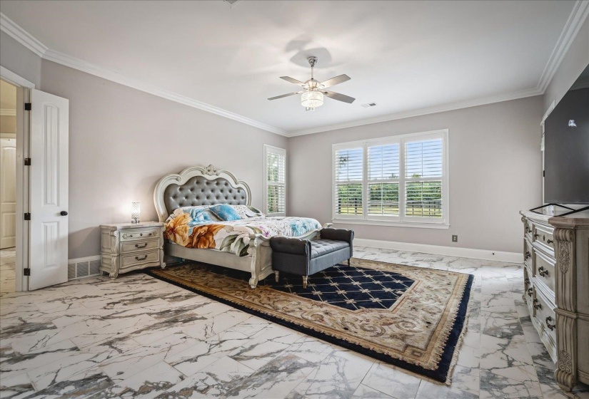 Spacious bedroom featuring large format tile flooring, crown molding, and a ceiling fan with integrated lighting