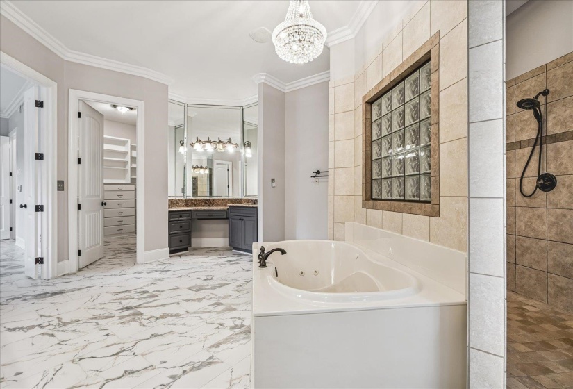 Spacious bathroom featuring marble-look tile flooring, a built-in jetted tub, a glass block window, a walk-in shower with tile surround, and a vanity area with multiple mirrors and built-in cabinetry