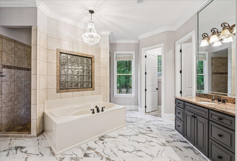 Spacious bathroom featuring a built-in soaking tub, glass block window, and separate tiled shower
