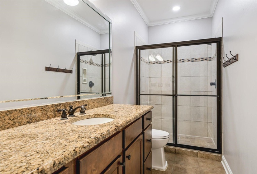 Bathroom featuring a granite-look countertop vanity with an undermount sink, bronze-finish faucet, framed mirror, and a shower with sliding glass doors, tile surround, and decorative accent band