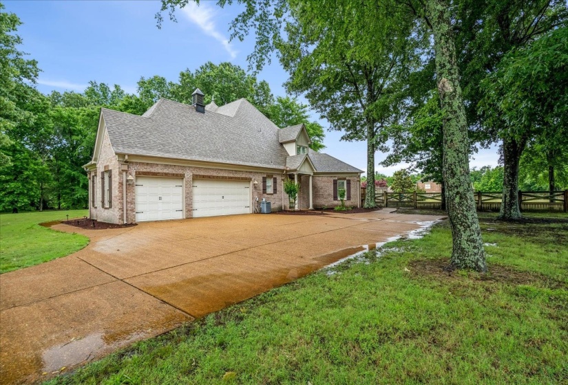 Brick exterior home featuring a two-car garage, pitched shingle roof, decorative cupola, and a wide paved driveway