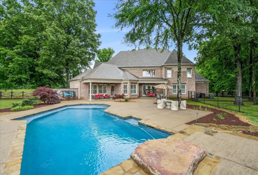 Expansive outdoor living area featuring a large inground swimming pool with stone coping, a spacious concrete patio, and a covered porch