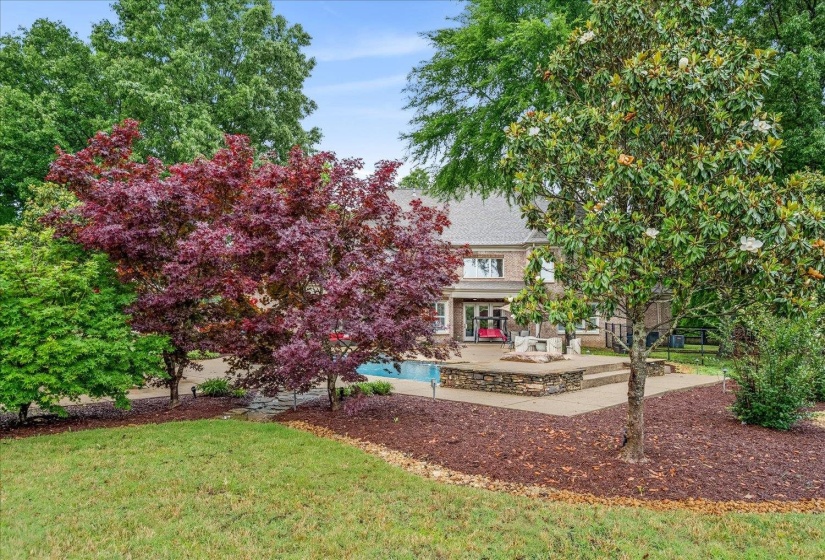 Expansive backyard featuring a blue swimming pool, stone patio, and tiered landscaping