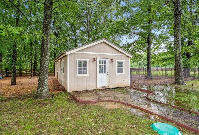 Freestanding outbuilding featuring a neutral-toned exterior, white trim windows, and a white paneled door