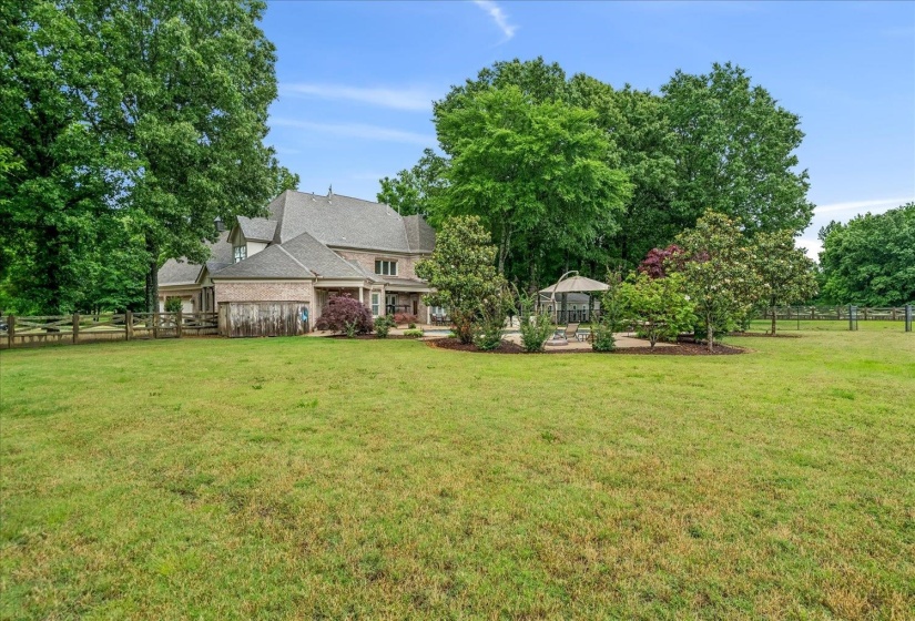 Expansive lawn with mature trees, a multi-story brick residence with a gabled roof, and a visible gazebo