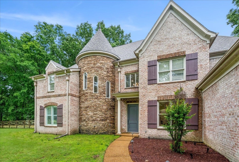 Traditional brick exterior featuring a stone turret with arched windows, dark shutters, and a covered entry