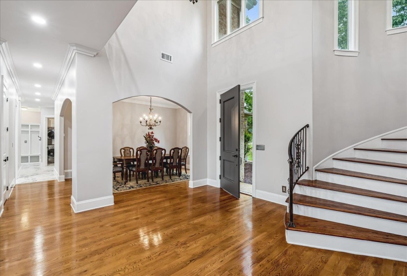 Two-story foyer with rich wood-finish flooring, a grand curved staircase featuring an ornate wrought iron railing, and a dark-paneled door