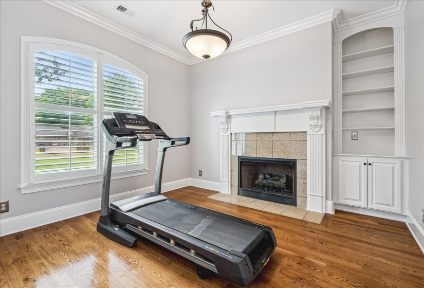 Arched windows with plantation shutters, a tiled fireplace with mantel, built-in shelving, crown molding, and wood-finish flooring