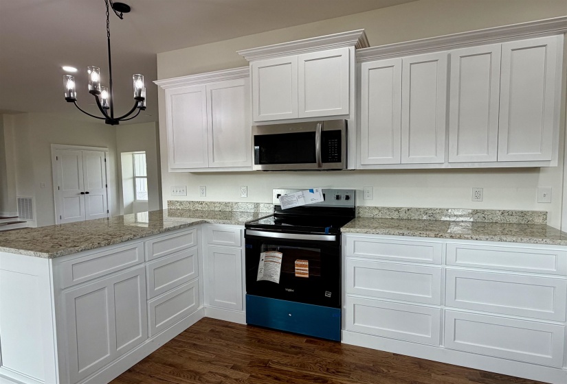 Kitchen with electric stove, stainless steel microwave, dark wood finished floors, white cabinetry, and light stone countertops