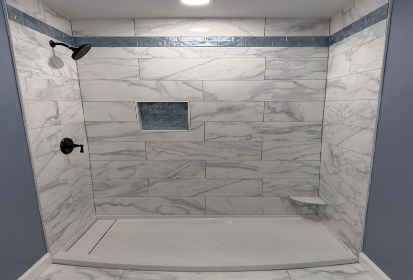 Tiled shower stall featuring white marble-look tiles, a blue glass accent tile band, and matte black fixtures