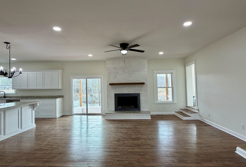 Unfurnished living room featuring dark wood-style flooring, a ceiling fan, a chandelier, and a fireplace